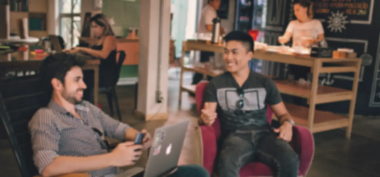 Two friends chatting in a café, one with a laptop