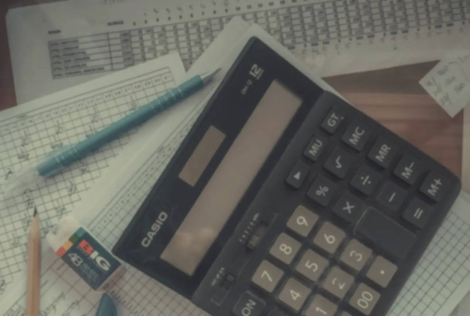 A calculator, pens and handwritten sums on paper