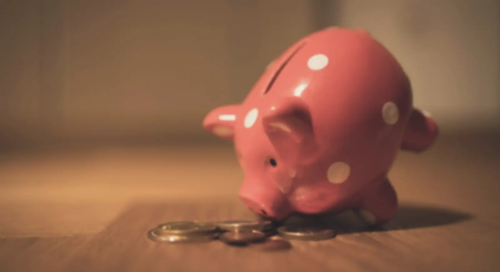 A red spotted piggy bank with a few coins beside it